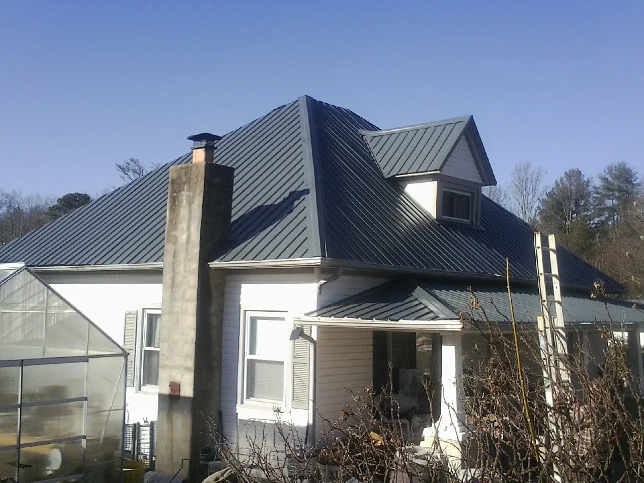 Dark blue standing seam metal roof on a white farmhouse with dormer — Slate & Tile Roof Repair by Roofing Brothers in Waveland