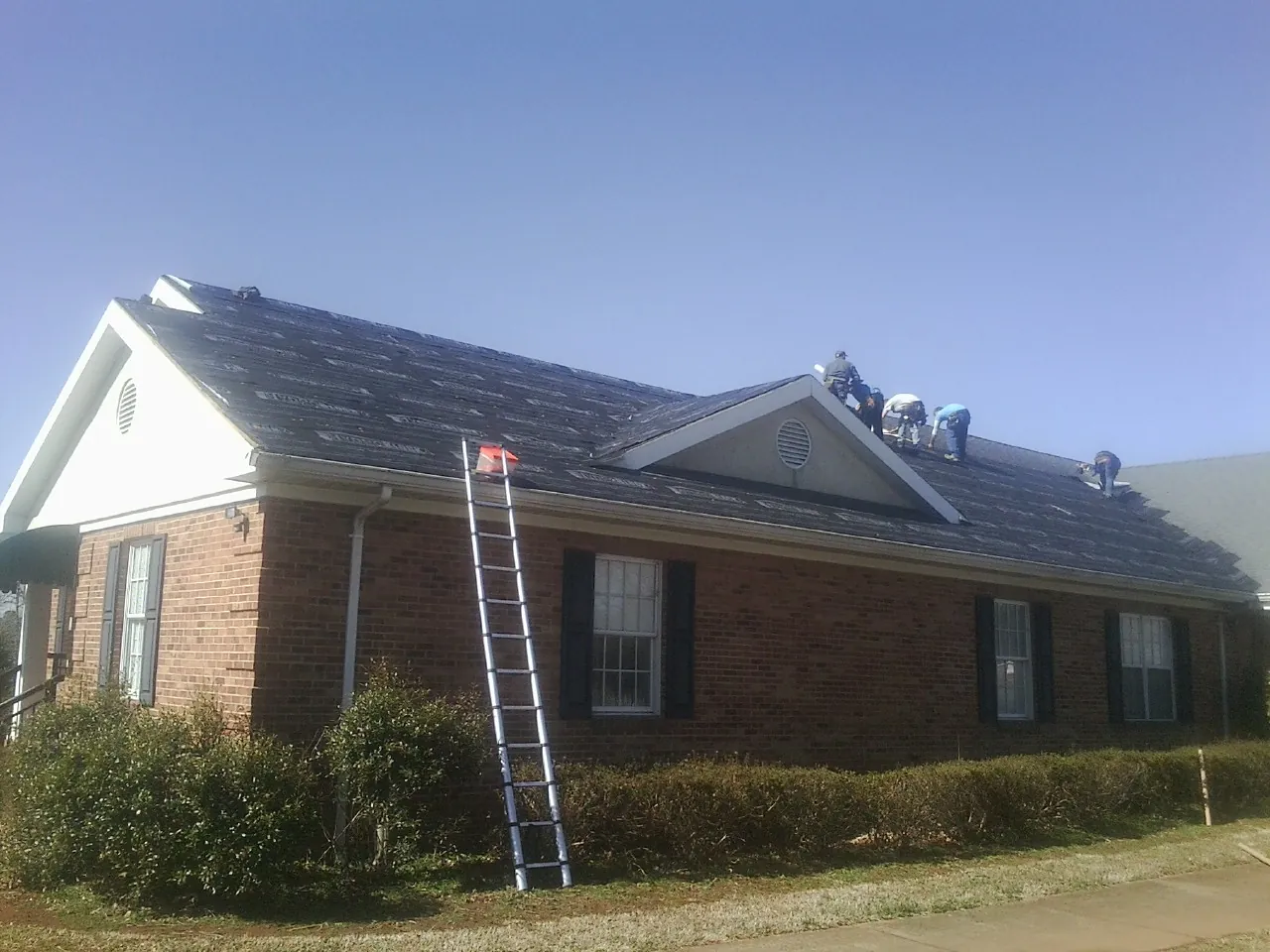 Crew tearing shingles off a brick ranch roof with a ladder set — Metal Roof Repair work by our crew in Waveland