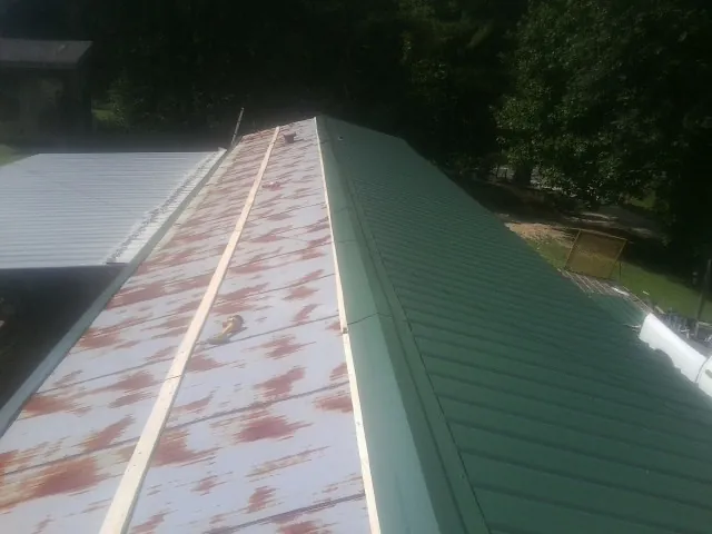 Old rusted panels beside newly installed green metal roofing — Wind Damage Roof Repair by Roofing Brothers in Waveland