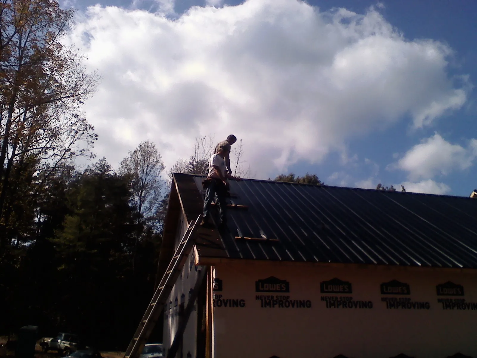 Roofer fastening dark metal panels high against a cloudy sky, from a Roof Inspection job in Waveland