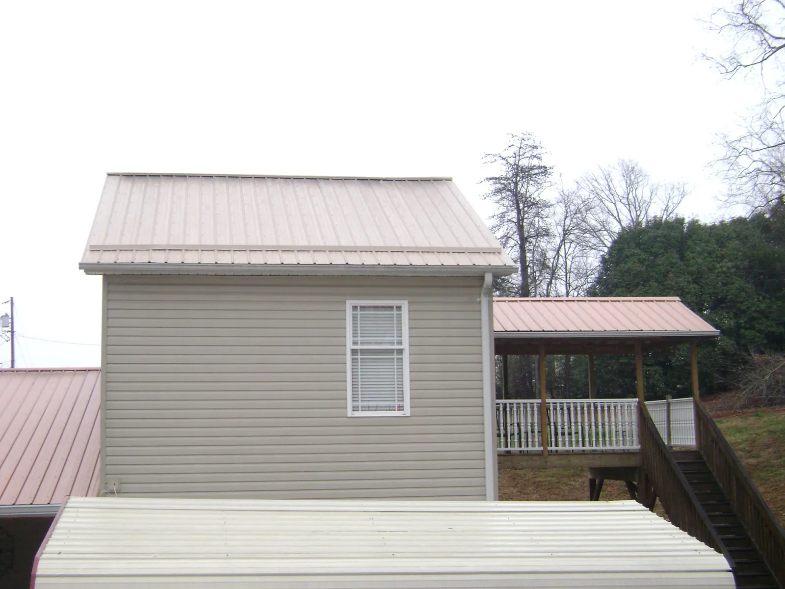 Tan metal roofs on a two story addition and attached porch, from a Roof Replacement job in Waveland